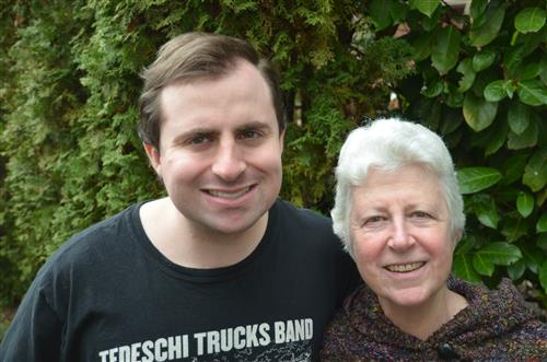 Young man in his 20's and his mother pose for a photo in front of green shrubs